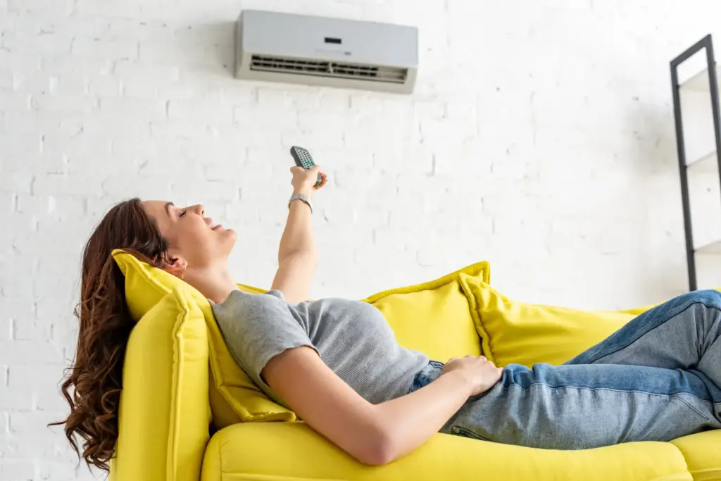 woman relaxing on a sofa, controlling an air conditioner with a remote
